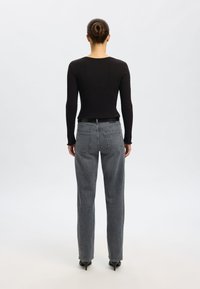 Fekete, bordázott mint�ájú hosszú ujjú felső, magas derekú, egyenes szárú szürke farmerral párosítva. Az öltözék minimalista stílusú, látható logók nélkül.