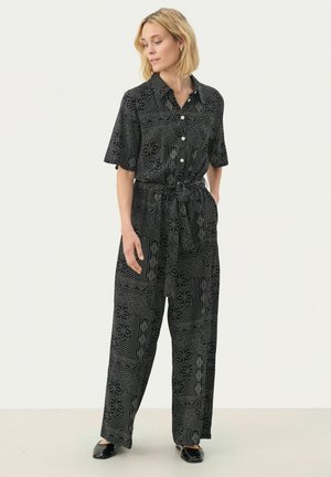 Black jumpsuit with short sleeves, button front, belt at the waist, and white geometric patterns throughout. Material appears lightweight and flowy.