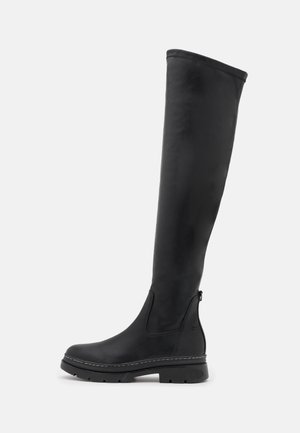 Musta polven yläpuolelle ulottuva saapas, jossa on paksu pohja, pyöreä kärki ja vetoketju takana, suunniteltu rentoon tai ulkoilukäyttöön.