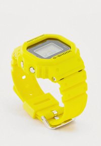 Kollane G-SHOCK digitaalne käekell ruudukujulise sihverplaadi, silikoonist rihma ja metallist pandlaga. Tekst sisaldab sõnu "PROTECTION" ja brändi logo.