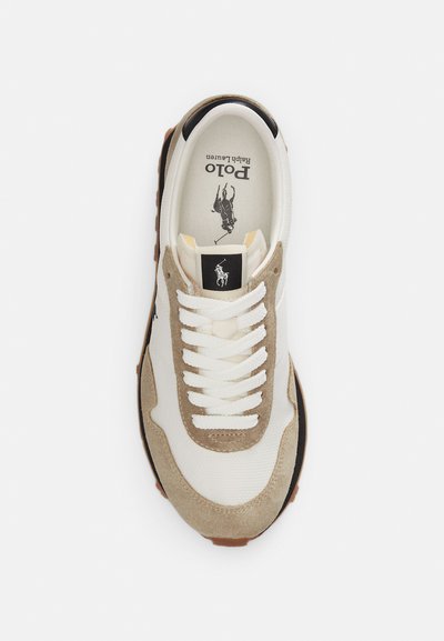 Άσπρο και μπεζ αθλητικό παπούτσι με άσπρα κορδόνια, μαύρο λογότυπο Polo Ralph Lauren στη γλώσσα και στη σόλα, φωτογραφημένο από πάνω σε λευκό φόντο.