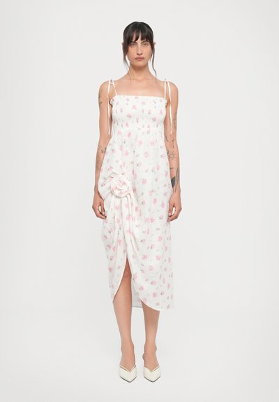 White, floral-patterned dress with adjustable straps, smocked bodice, and side twist detail. Ankle-length with a front slit.