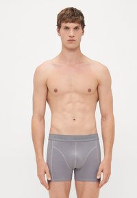Young man standing facing forward wearing gray Jack & Jones boxer briefs against plain white background.