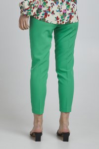 Groene op maat gemaakte broek met enkel lengte, slim fit ontwerp, en een gladde textuur. Draagt een top met bloemenpatroon en zwarte blokhak sandalen.