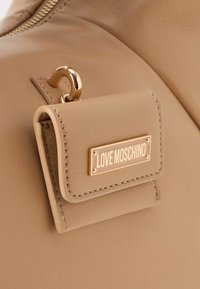 Beige odos rankinė su mažą prijungtu maišeliu, kuriame yra auksinė "Love Moschino" logotipo plokštelė ir auksinė aparatūra.