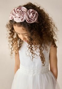 Un bandeau en satin rose orné de trois embellissements en forme de rose, porté par un enfant aux cheveux bouclés, sur un fond neutre.