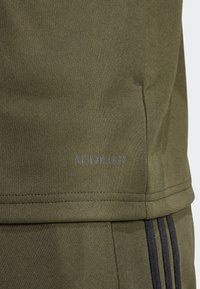 Olive green athletic top with textured fabric, featuring a "AEROREADY" logo in grey and contrasting black stripes along the side.