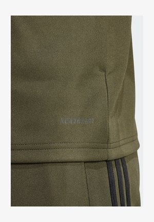 Oliven grøn træningstop med struktureret stof, der har et "AEROREADY" logo i grå og kontrasterende sorte striber langs siden.