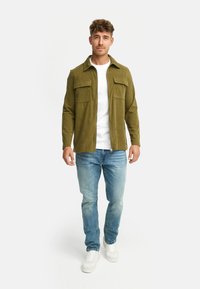 Oliven grøn fløjl skjortejakke med to brystlommer, parret med lyseblå jeans og hvide sneakers, med lynlås foran og krave.