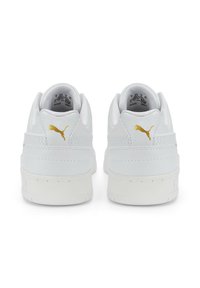Weiße Sneakers aus strukturiertem Leder, flachen weißen Sohlen und goldenen Puma-Logo-Akzenten an der Ferse. Minimalistisches Design mit abgerundetem Zehenbereich und niedrigem Profil.