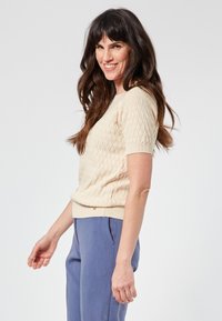 Short-sleeve knit sweater in light beige with textured diamond pattern and ribbed hem, paired with light blue tailored trousers.