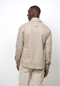 Beige langslivend shirt met een gespreide kraag, textuurstof en knoopmanchetten, met een gebogen zoom en details van het achterpand.
