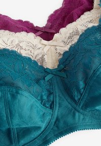 Drie beha's in donkerpaars, crème en teal met kantdetail. Elke beha heeft een strikaccent in het midden en textuurstoffen.