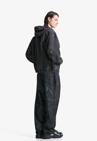 Zwart denim hoodie jack met een relaxte pasvorm, elastische manchetten en tailleband, gecombineerd met losse zwarte broeken met een gestructureerde afwerking.
