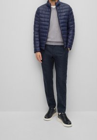 Doudoune navy, pull gris, pantalon texturé foncé, baskets noires. La doudoune présente un design matelassé et un col haut.