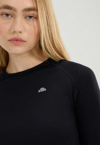 Zwarte lange mouwen sporttop met een gestructureerd patroon en een klein grijs logo op de borst. Glad afwerking. Close-up weergave.