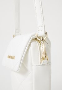 Λευκή τσάντα από κουνιστό δέρμα με κλείσιμο τύπου καπάκι, χρυσό φερμουάρ με επωνυμία και λεπτό ρυθμιζόμενο λουρί. Λείος υφή με διακοσμητικά στοιχεία.