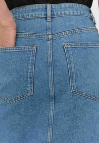 Blå denimkjol med en åtsittande midja, som har två bakfickor och en slät yta. Sömmen i en kontrasterande färg framhäver designen.