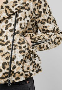 Kurtka w wężowy wzór z teksturowanej tkaniny z czarnymi zamkami błyskawicznymi, z ukośnym zapięciem na zamek i akcentami bocznych kieszeni.