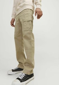 Beige cargo byxor med flera fickor, rak ben-design, synliga sömdetaljer, kombinerat med svartvita sneakers.