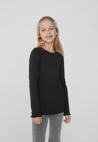 Czarna, długorękawowa, żebrowana bluzka z okrągłym dekoltem i postrzępionym wykończeniem. Połączona z szarymi dżinsami, prezentuje swobodny krój i luźny styl.