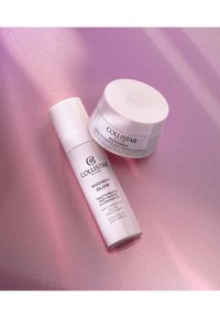 Collistar hudvårdsprodukter på en rosa glittrande yta. Inkluderar en vit pumpflaska och en vit krämburk, båda med minimalistisk design och etiketter.