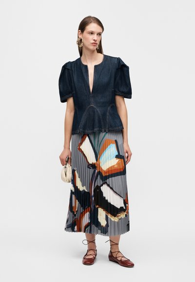 Τζιν τοπ με φουσκωτά μανίκια, βαθύ V ντεκολτέ και διακοσμητικές ραφές· πλισέ μάξι φούστα με λουλουδάτο μοτίβο σε γκρι αποχρώσεις· καφέ μπαλαρίνες.