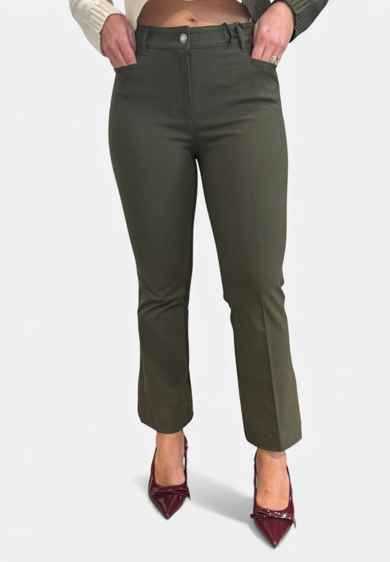 Olijfgroene taps toelopende broek met een gladde textuur, zakken aan de voorkant en een knoopsluiting, gecombineerd met glanzende bordeauxrode hoge hakken.