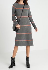 Grå stickad klänning med horisontella orangea ränder, långa ärmar och rundad halsringning. Matchad med svarta ankelstövlar och en svart väska.