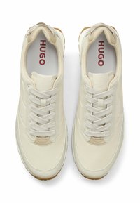 Zapatilla cremosa con textura suave, cordones visibles y un logo sutil en el costado. Cuenta con suela de goma y collar acolchado.