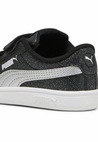 Baskets noires avec une texture scintillante, dotées d'un logo Puma blanc, d'une bande latérale blanche contrastante et d'une fermeture à scratch.