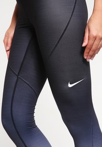 Mallas deportivas negras con un diseño ajustado, que presentan un sutil degradado, tejido texturizado y un logotipo de Nike en blanco en la parte inferior de la pierna izquierda.