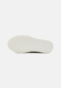 Weiße Gummisohle mit strukturierten Grip-Mustern und Branding. Hat ein flaches Design mit horizontalen und vertikalen Rillen für Traktion.