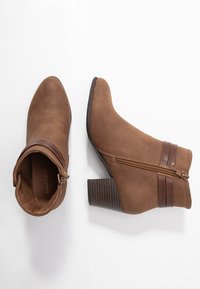 Brązowe botki za kostkę wykonane z zamszu, z ostro zakończonym noskiem, zamkiem błyskawicznym oraz brązowymi skórzanymi akcentami i słupkowym obcasem.