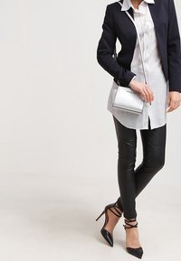 Blazer marino sobre una camisa blanca, leggings de cuero negros y tacones negros de punta con correas en el tobillo. Pequeño bolso cruzado plateado.