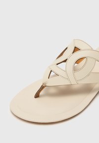 Sandale din piele bej cu design decupat, bareta subțire pentru degetul mare și accente cusute. Talpă plată cu o ușoară curbură și finisaj natural.