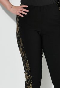 Zwarte broek met gouden bloemenborduursels langs de zijkant, gemaakt van zachte stof met een elastische tailleband voor comfort.