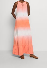 Vestido maxi en degradado coral, con cuello halter, detalle de lazo, dobladillo con volantes en capas y tejido suave. Combinado con sandalias de tiras marrones.