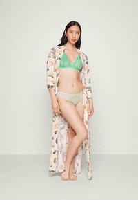 Robe floral longa com um tecido suave e leve; modelo usa um sutiã de renda verde e roupa interior combinando; fundo neutro.