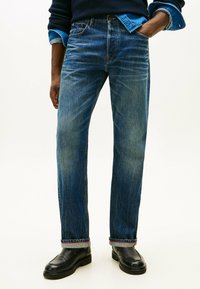 Jeans in denim blu con vestibilità a gamba dritta, sbiadito visibile e cuciture a contrasto all'orlo. Abbinati a scarpe in pelle nere.