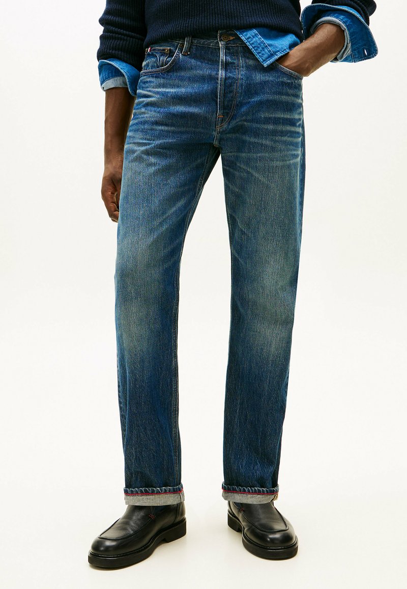 Jeans in denim blu con vestibilità a gamba dritta, sbiadito visibile e cuciture a contrasto all'orlo. Abbinati a scarpe in pelle nere.