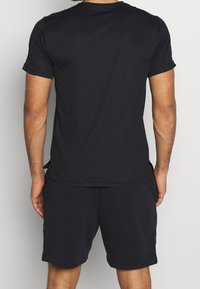 Czarna sportowa koszulka z gładkiego materiału, z krótkimi rękawami i okrągłym dekoltem, w połączeniu z dopasowanymi czarnymi szortami.