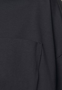 Schwarzes Baumwoll-T-Shirt mit lässiger Passform, das eine strukturierte Oberfläche und eine horizontale Naht hat, die die Vorderseite betont.