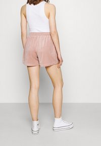 Shorts en velours rose à taille élastique, présentés de dos. Assortis à des baskets montantes blanches, sur un fond neutre.