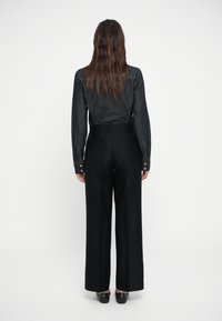 Donkere spijkerblouse met lange mouwen, gecombineerd met hoog-getailleerde zwarte broek met op maat gemaakte achterdetails en wijde pijpen.