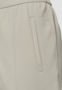 Lichtgrijze broek met een gestructureerde stof, elastische tailleband en een zijzak met subtiele stikseldetails.