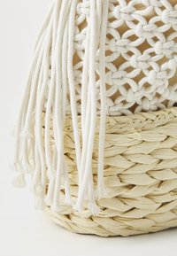 Panier en paille tressée avec une doublure en tissu beige, orné d'accents en corde blanche tressée et de détails en franges, texturé avec une finition naturelle.