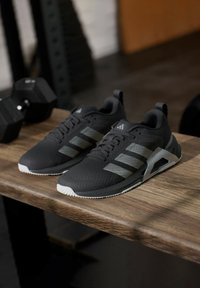 Chaussures de sport noires avec des rayures grises et des semelles en caoutchouc sur une surface en bois, avec une tige texturée et un design distinctif au talon.