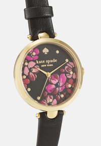 Reloj con correa de cuero negro y bisel en tono dorado, que presenta una esfera floral oscura decorada con flores rosas y marcadores de hora dorados. Destaca el logo de espade.