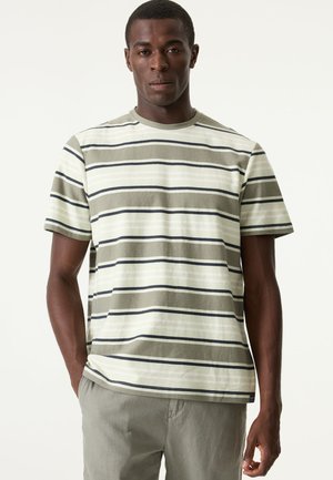 Maglietta a righe verdi con maniche corte; presenta righe orizzontali in varie sfumature di verde, bianco sporco e blu scuro. Tessuto in cotone.